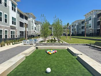 A grassy area with a ball and a row of multicolored balls in front of apartment buildings at The Quinn Luxury Apartments, Florida